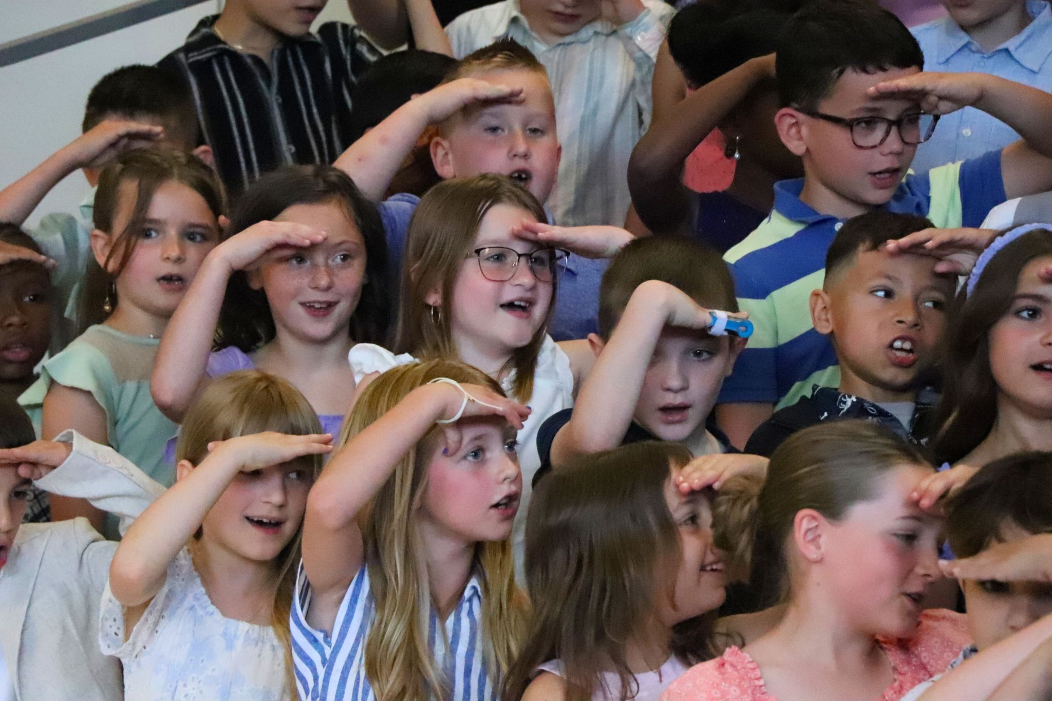 A group of students are looking around the room at the second grade moving up ceremony. 