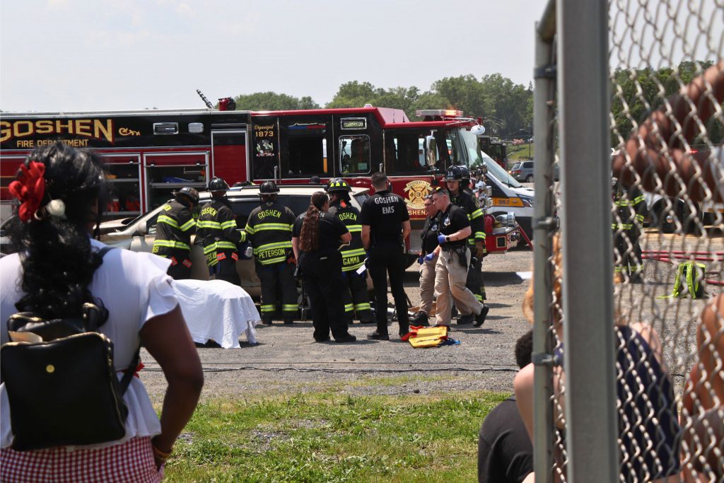 Students watch the mock crash simulation from the bleachers as fire fighters and medical personnel are attending to a car.