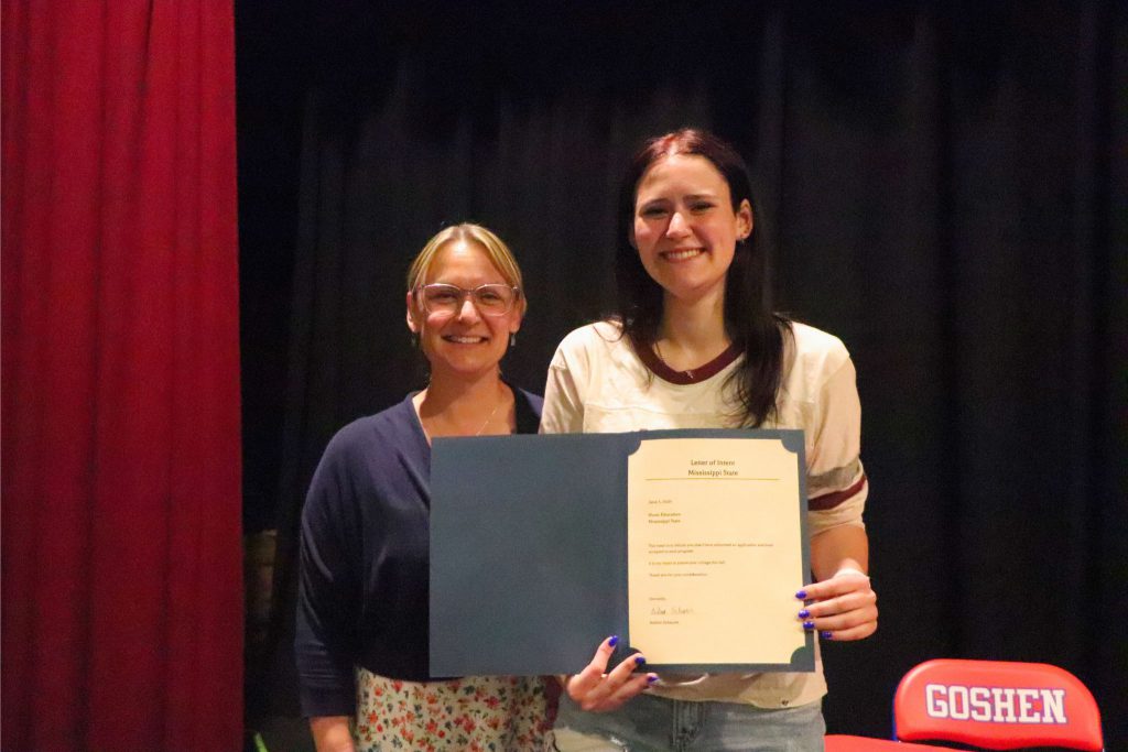 A student and a teacher smile with a letter in front of the table with Goshen chairs.