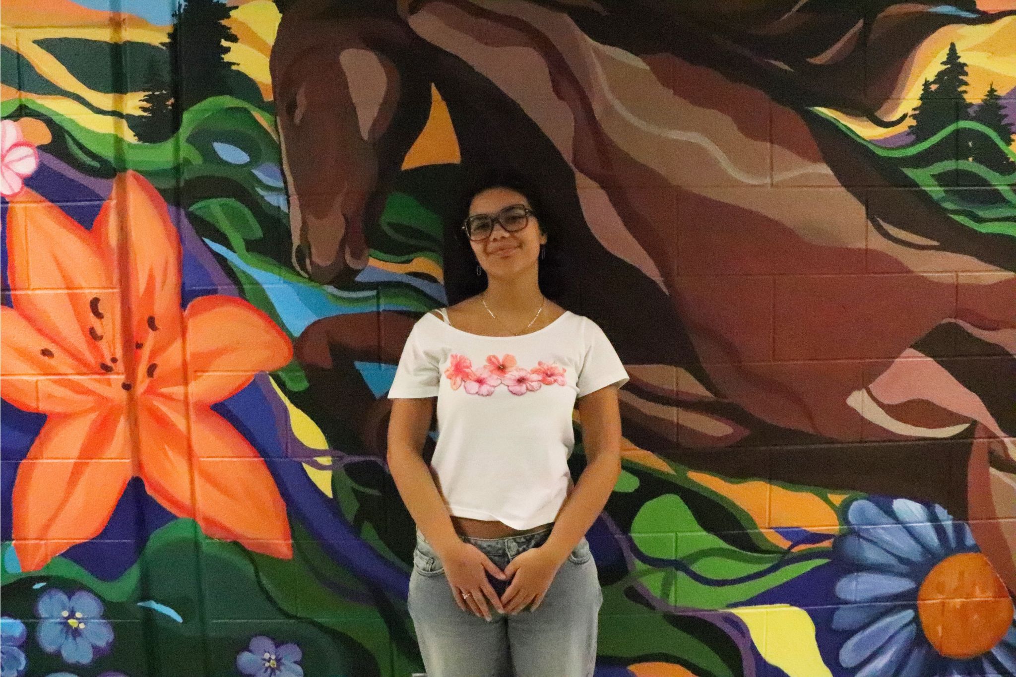Katie Palau stands in front of the mural she created on the wall in Goshen High School and smiles. The horse she painted is behind her.