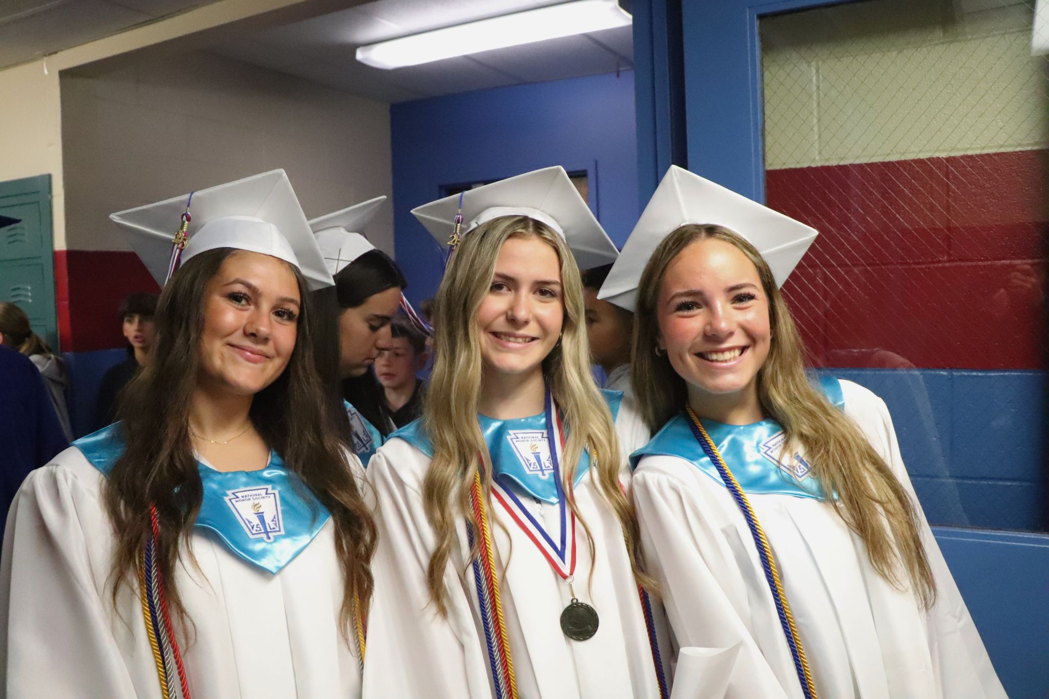 Three students smile and look at the camera during the senior walk through, 
