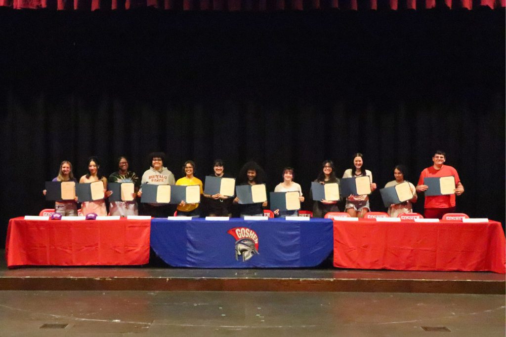 A group photo of students holding up their letters of intent to go to college at a table on stage in Goshen High School.