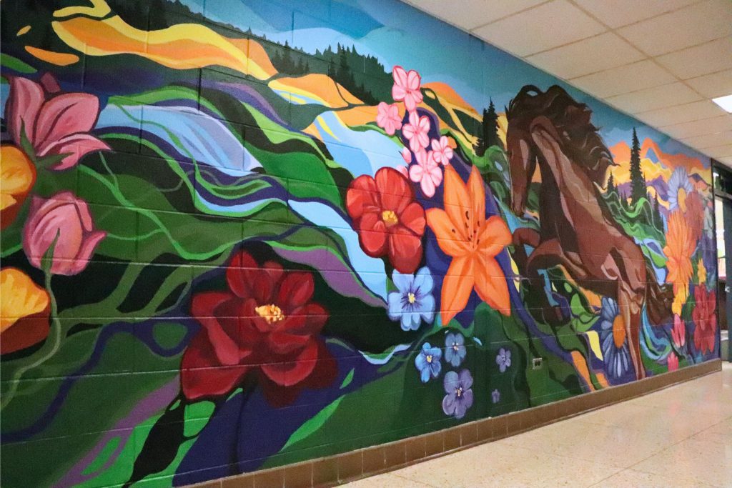 A finished side angle of the mural in Goshen High School. A horse is in the middle of flowers, and blue sky.