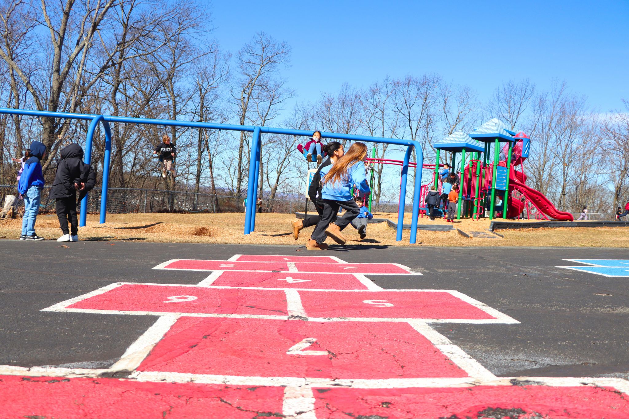 Students are running and playing at the playground with hop scotch in the foreground. 