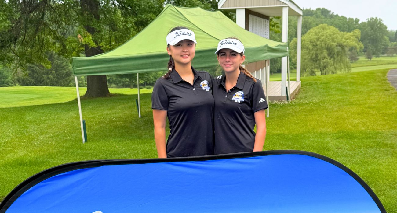 Two golf athletes stand behind a sign that says NYSPHAA Championships New York State Public High School Athletic Association