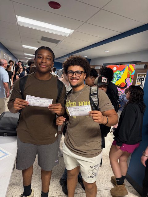 Two students smile with their gift certificates from Trail Side treats in the hallway at Goshen High School. 