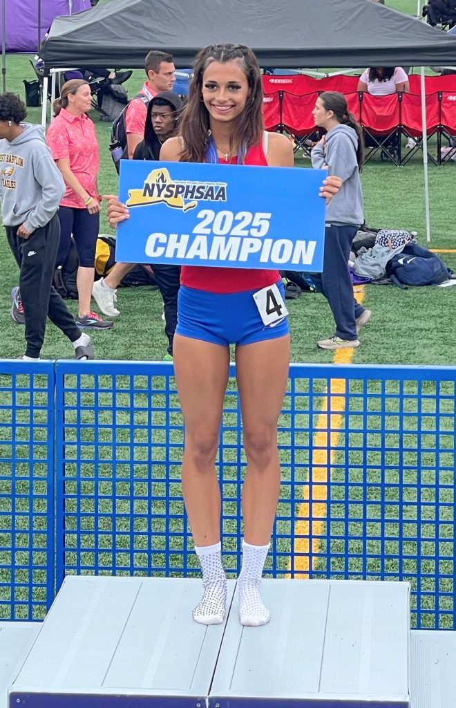 Joy Sawyer smiles for the camera and hods up a sign that says 2025 champion on it after winning her event.