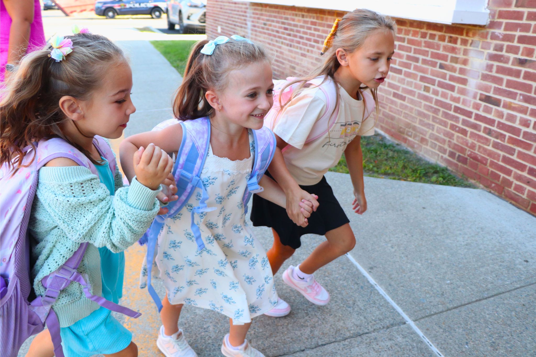 Three students hold hands and walk into school together on the first day of school.