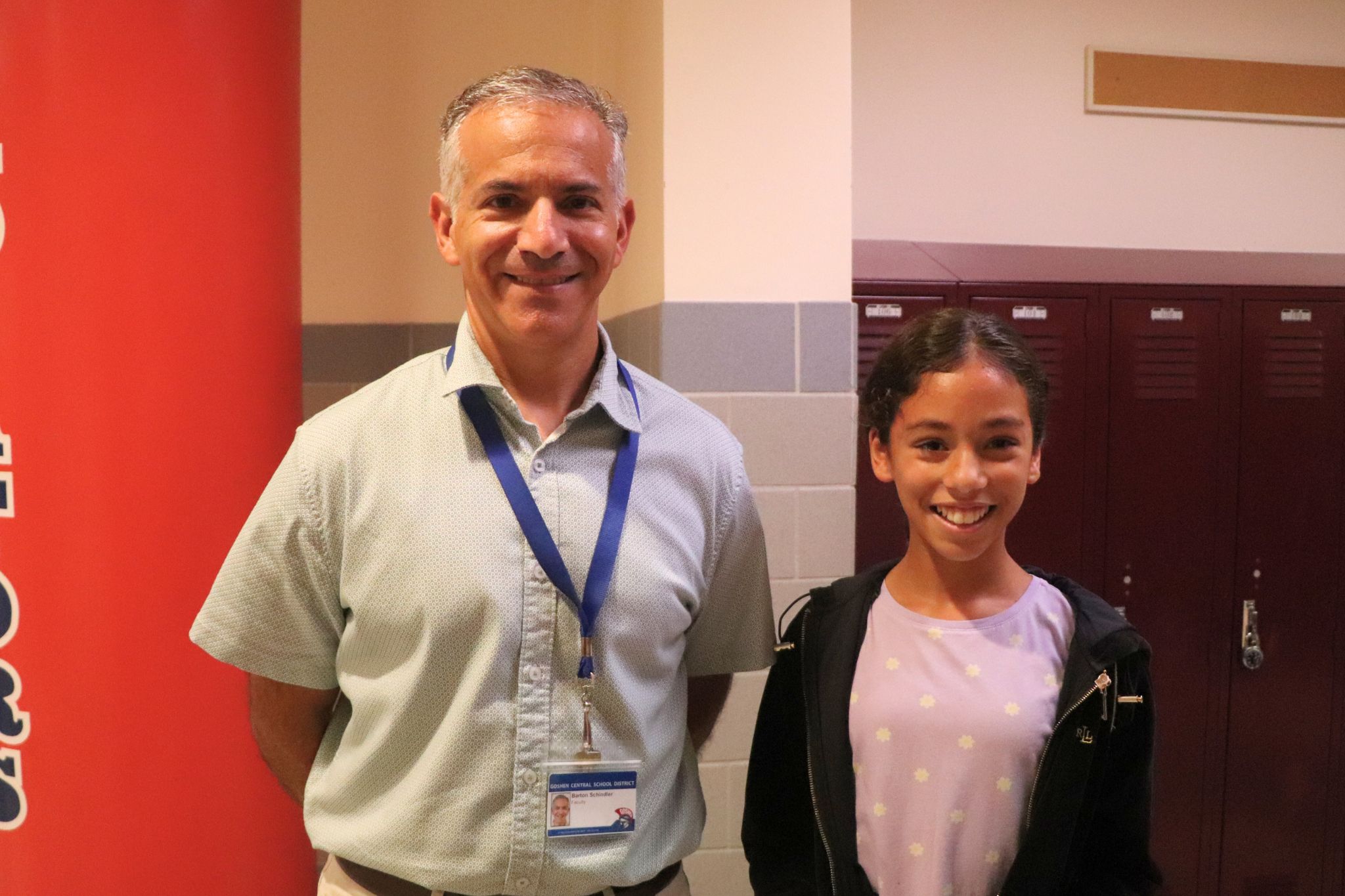 A student and a teacher smile and look at the camera in the middle school. 
