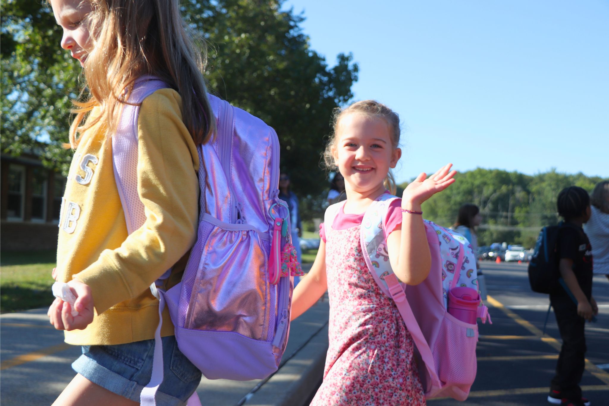 A student waves to the camera on their way in on the first day of school. 
