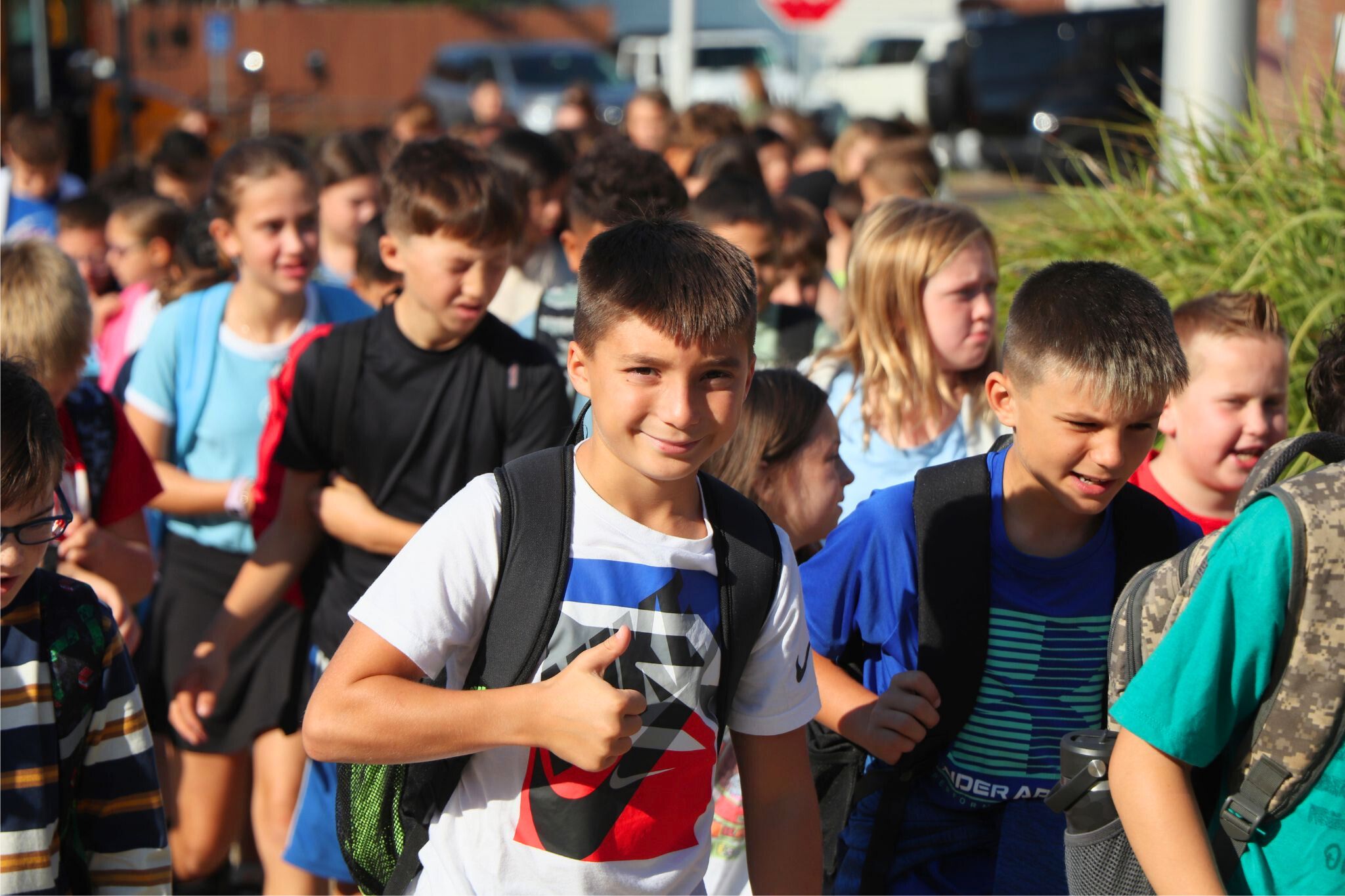 A student smiles and gives a thumbs up on their way into school.