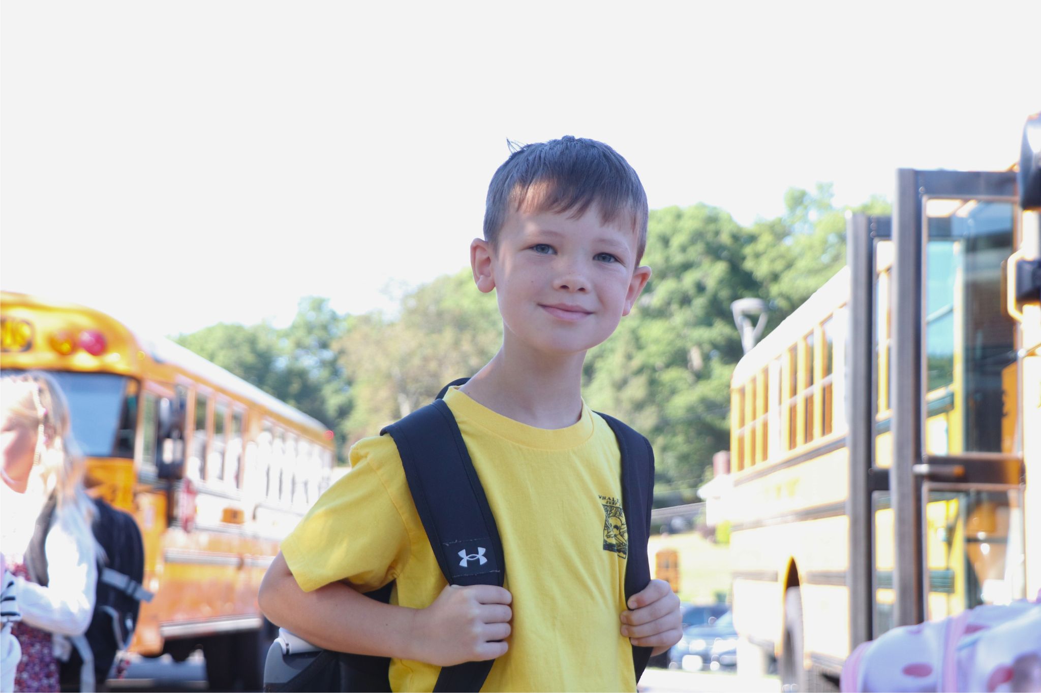 A student smiles for the camera in front of buses. 