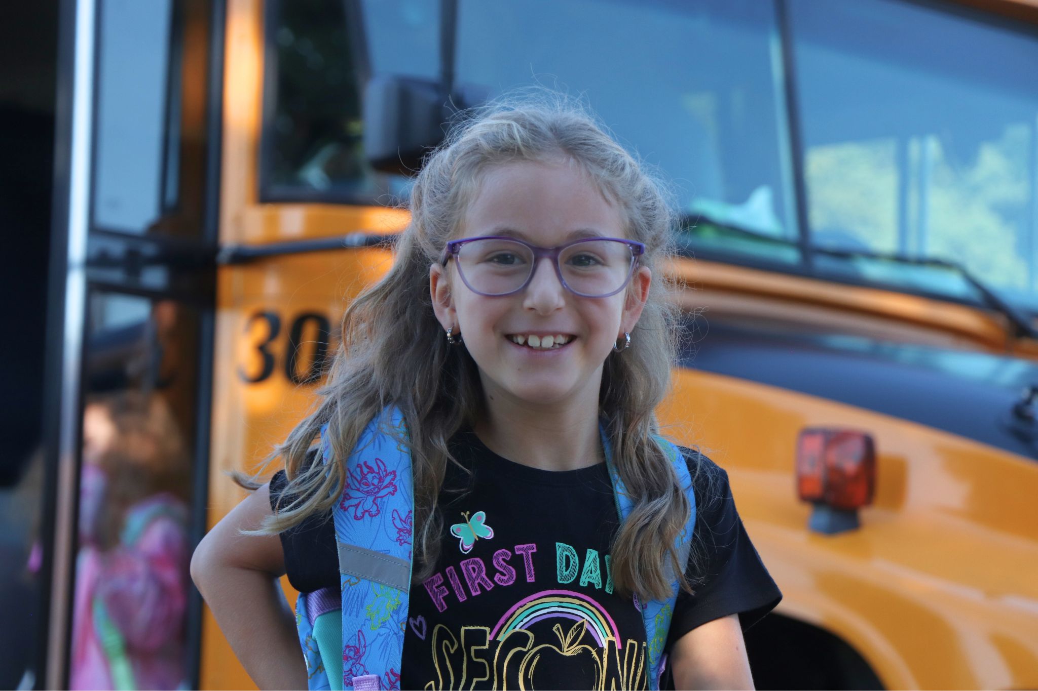 A student smiles for the camera in front of a bus. 