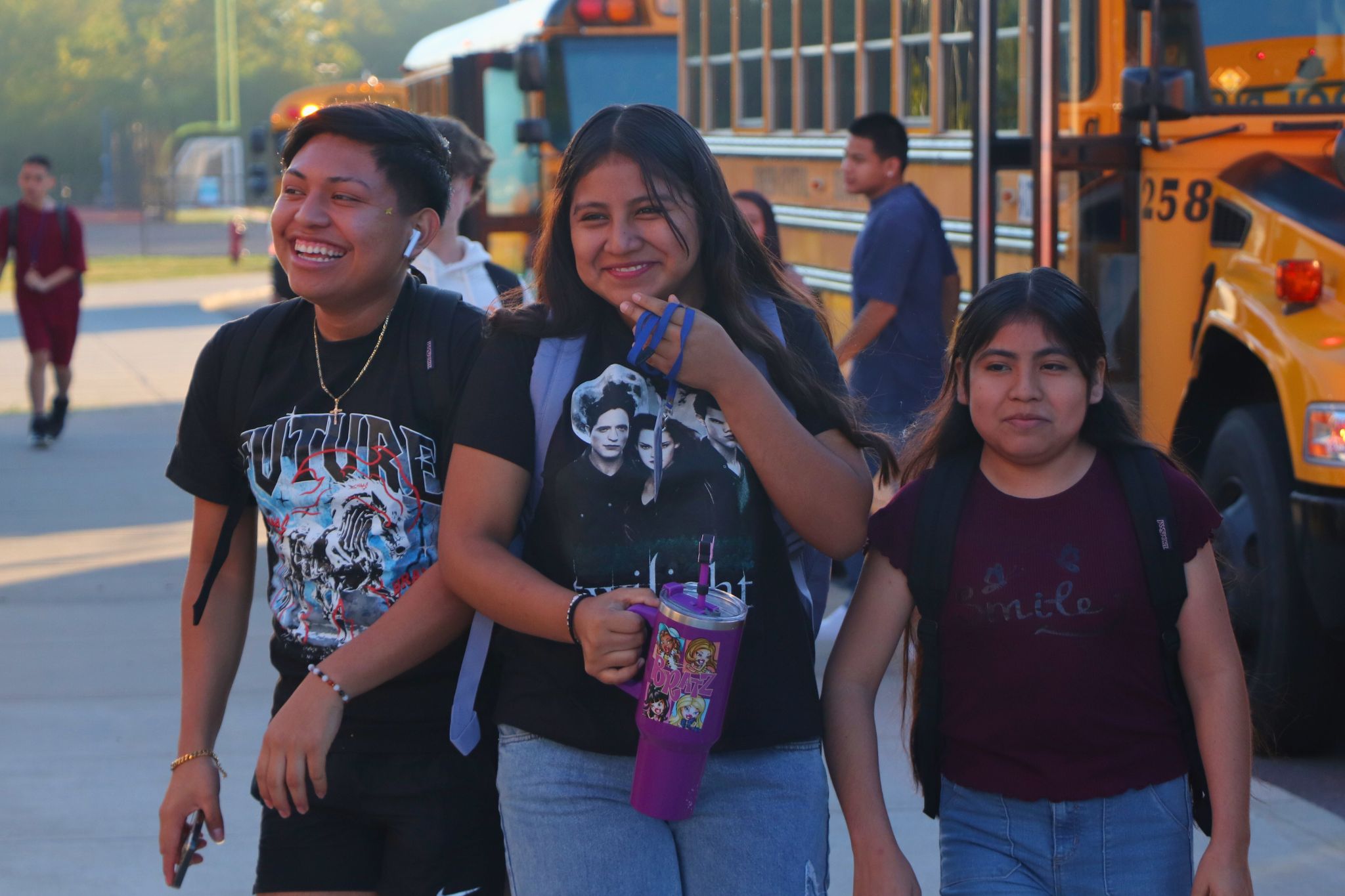 Three students smile and walk together into school on the first day. 