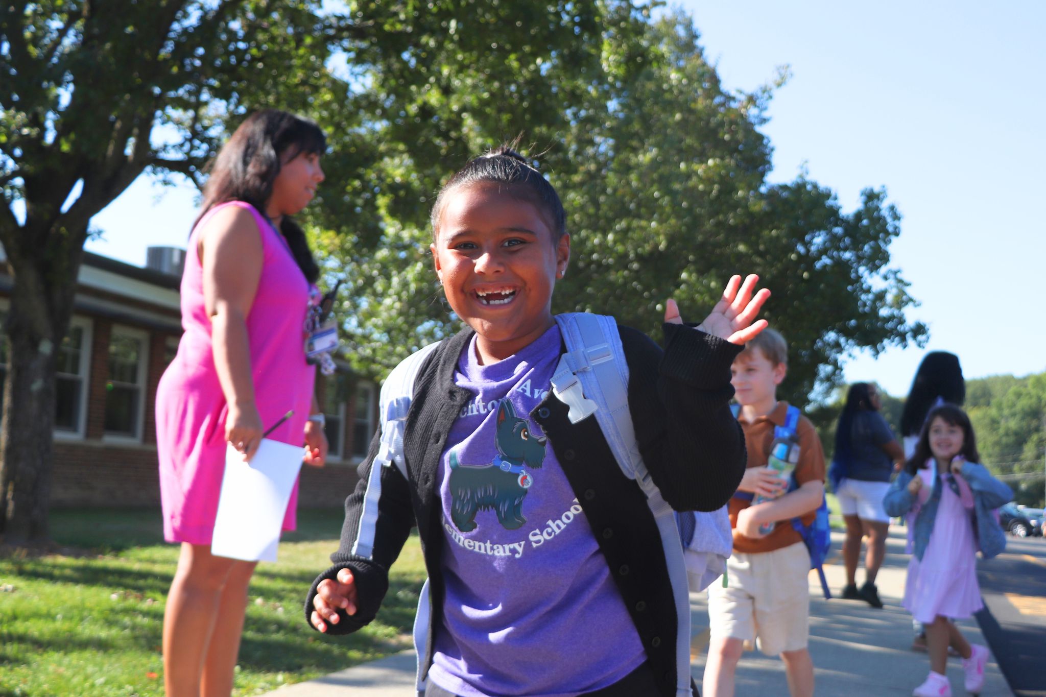 A student smiles and waves at the camera on the first day of school. 