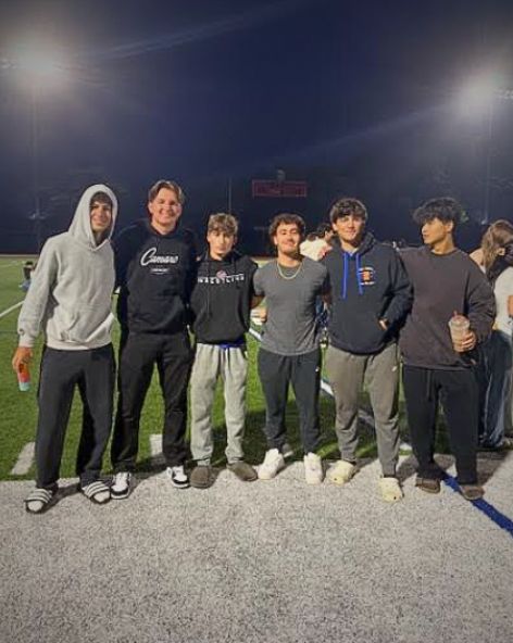 A group of Goshen High School seniors stand for a photo on the football field. They are smiling for a photo.