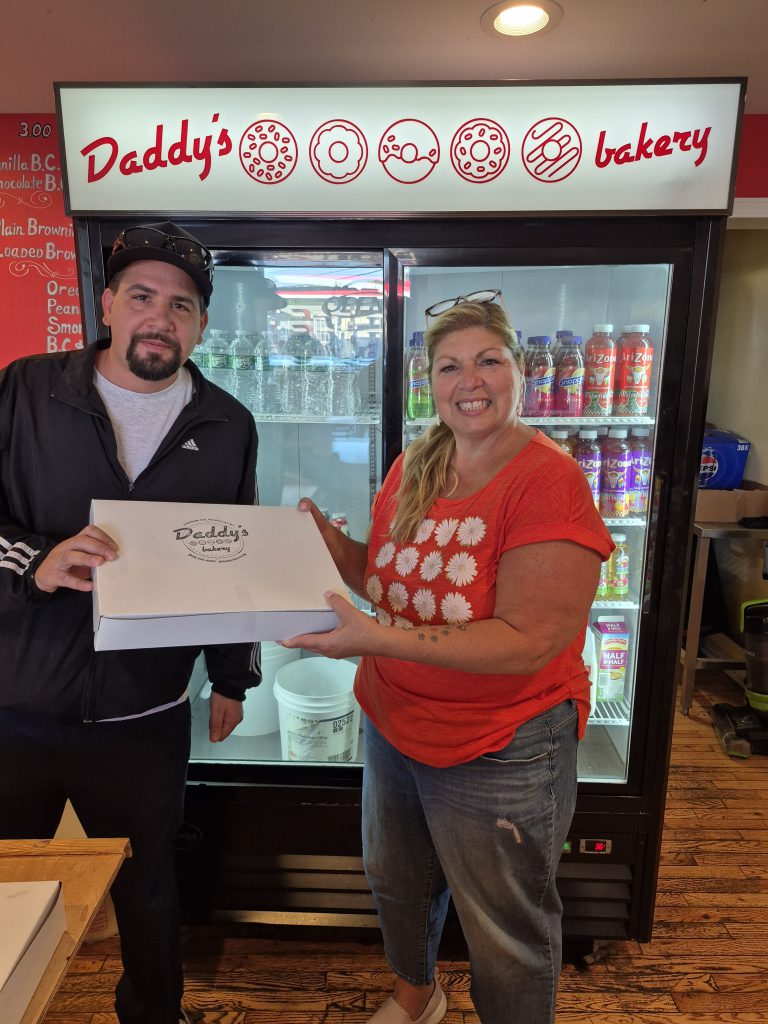 Two people hold a box of Daddy's Donuts in the bakery that was donated for custodian appreciation day.
