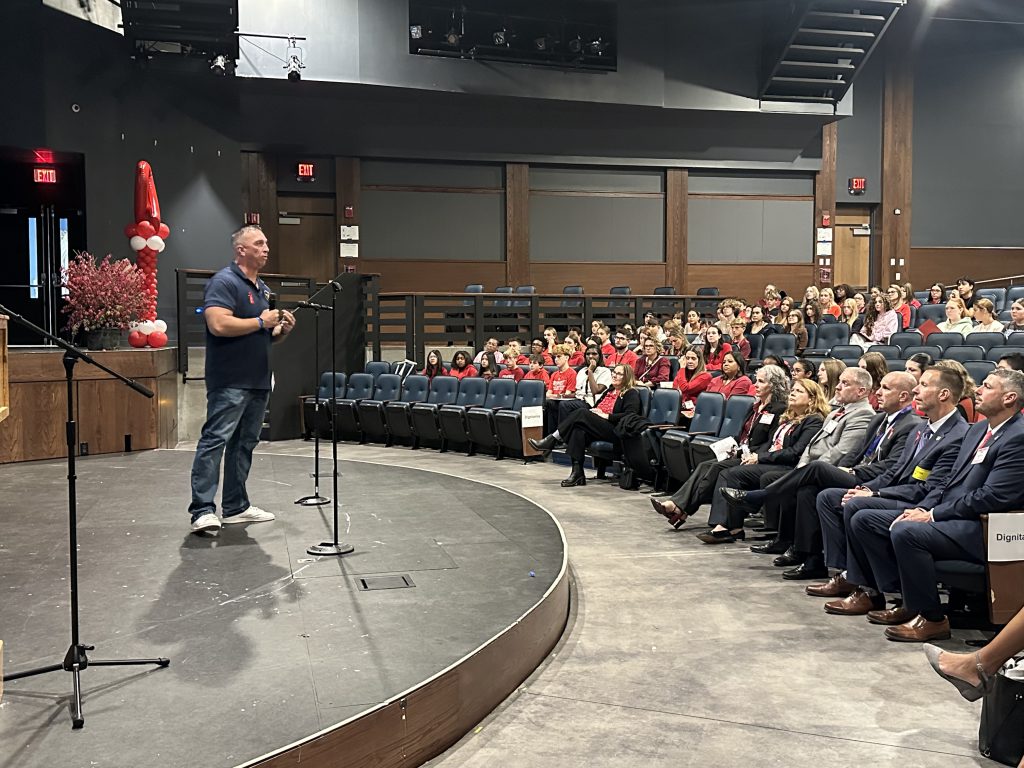 An adult speaks to an audience in a high school auditorium.