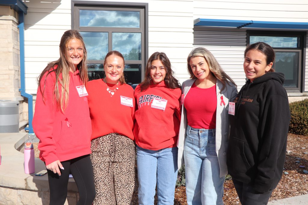 Teachers and students wearing red stand outside the high school smiling.