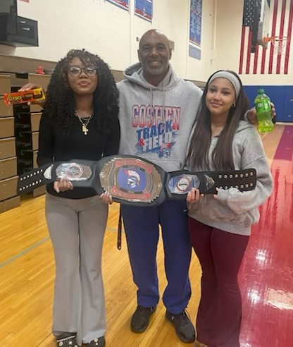 An adult stand with two students in a high school gym