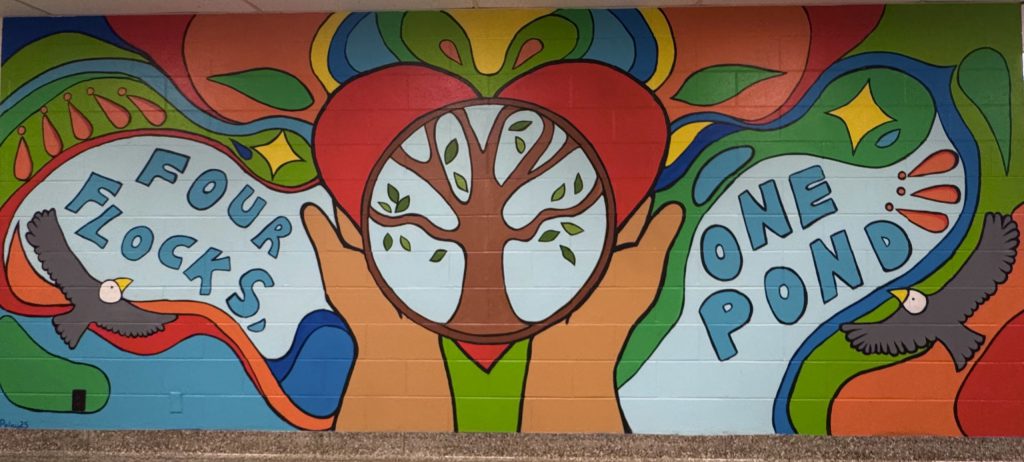 A painted mural on the wall of a school that says Four Flocks, One Pond