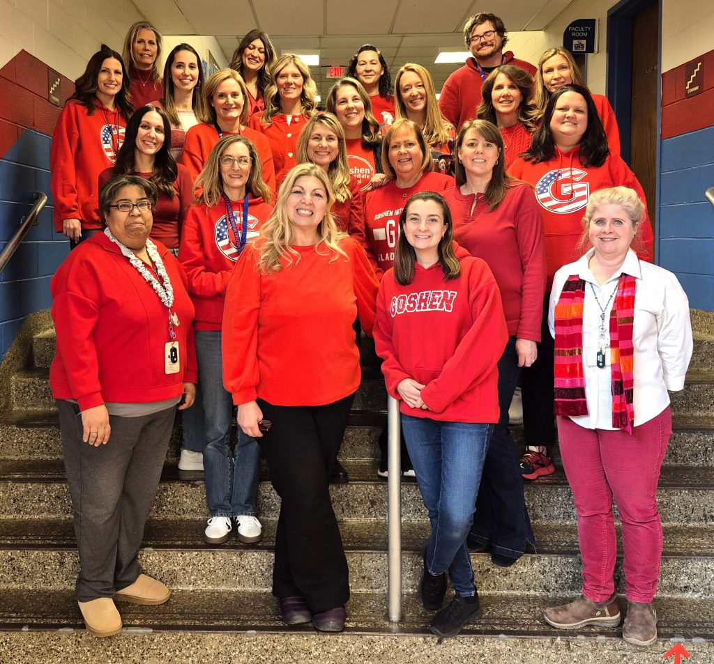 Adults stand on stairs inside a school. Many are wearing red.