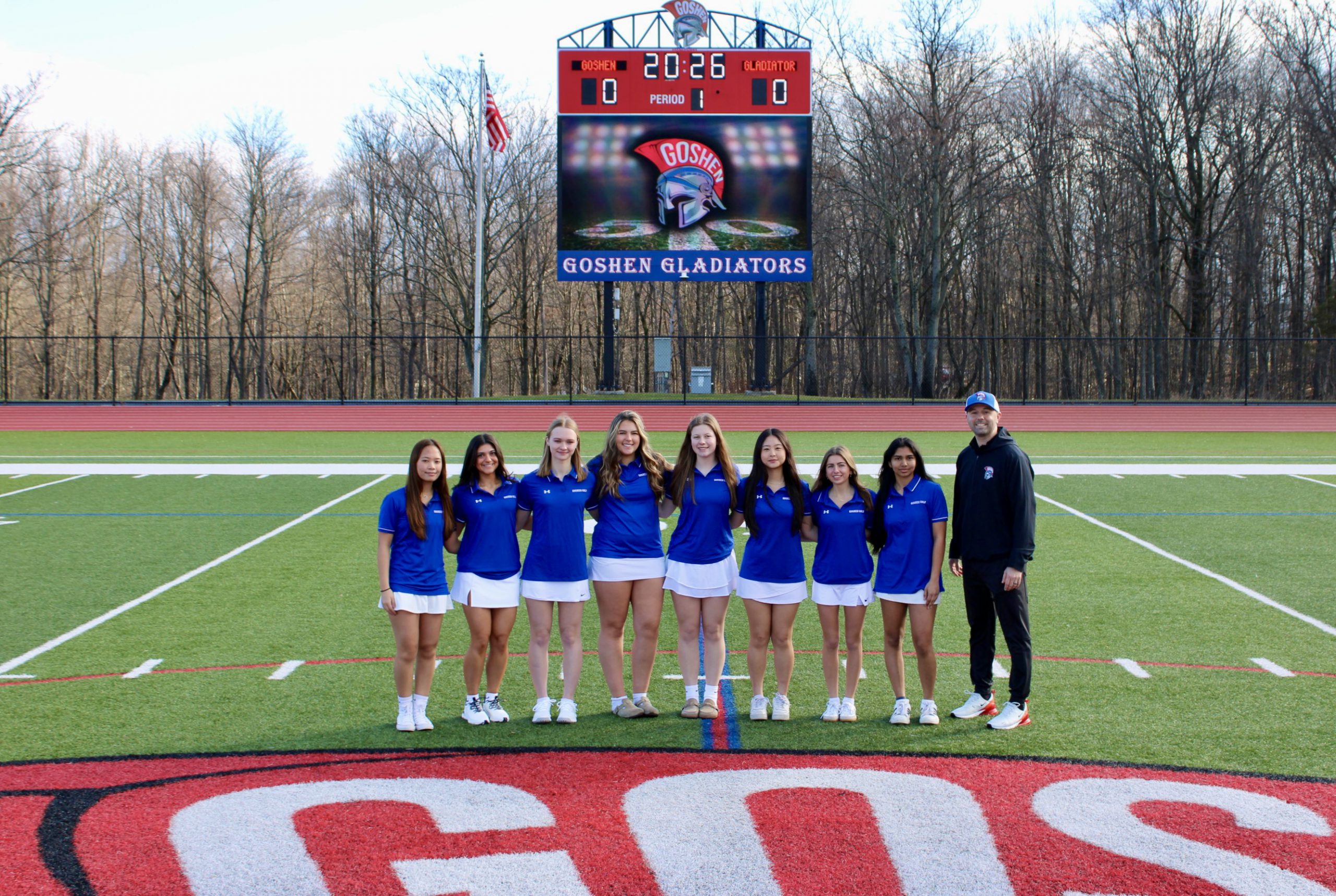 The Goshen Girls Varsity basketball team poses for their team photo. There is a row in front kneeling down and a row behind standing. The coaches are on the sides of the team.